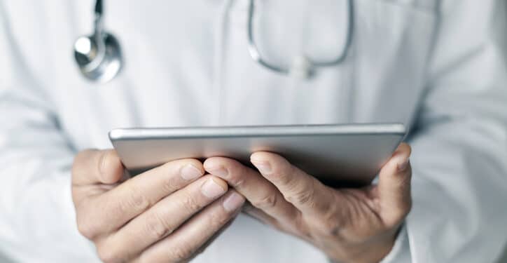 closeup of a young caucasian doctor man wearing a white coat using a tablet computer